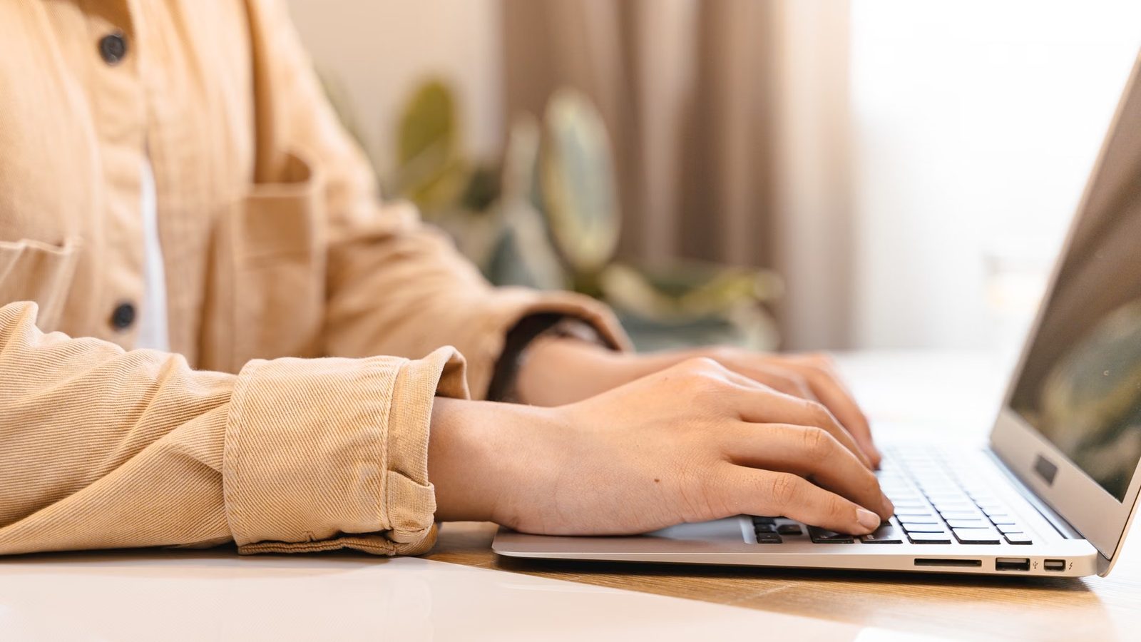 Dłonie piszące na klawiaturze laptopa przy jasnym biurku