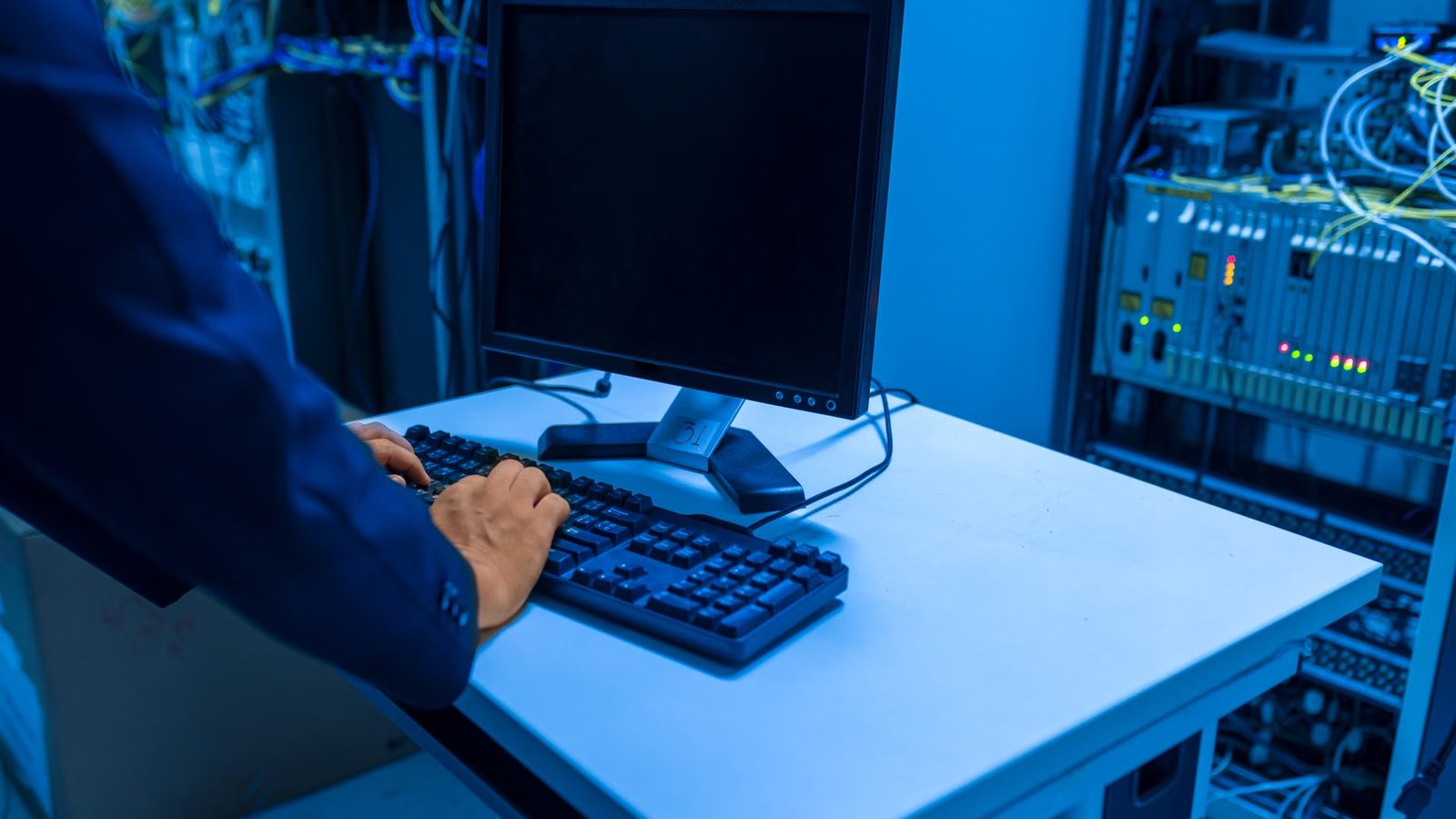 Technik pisze na klawiaturze laptopa ustawionego w serwerowni obok szaf z urządzeniami