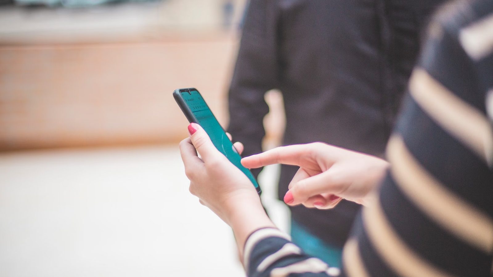 Jedna osoba trzyma telefon, druga wskazuje palcem na jego ekran