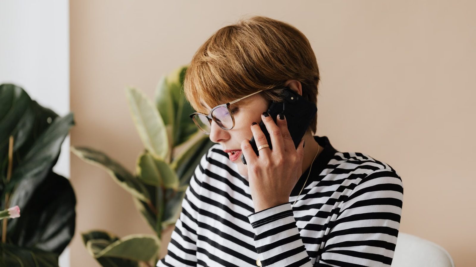 Kobieta w okularach rozmawia przez telefon komórkowy przy biurku