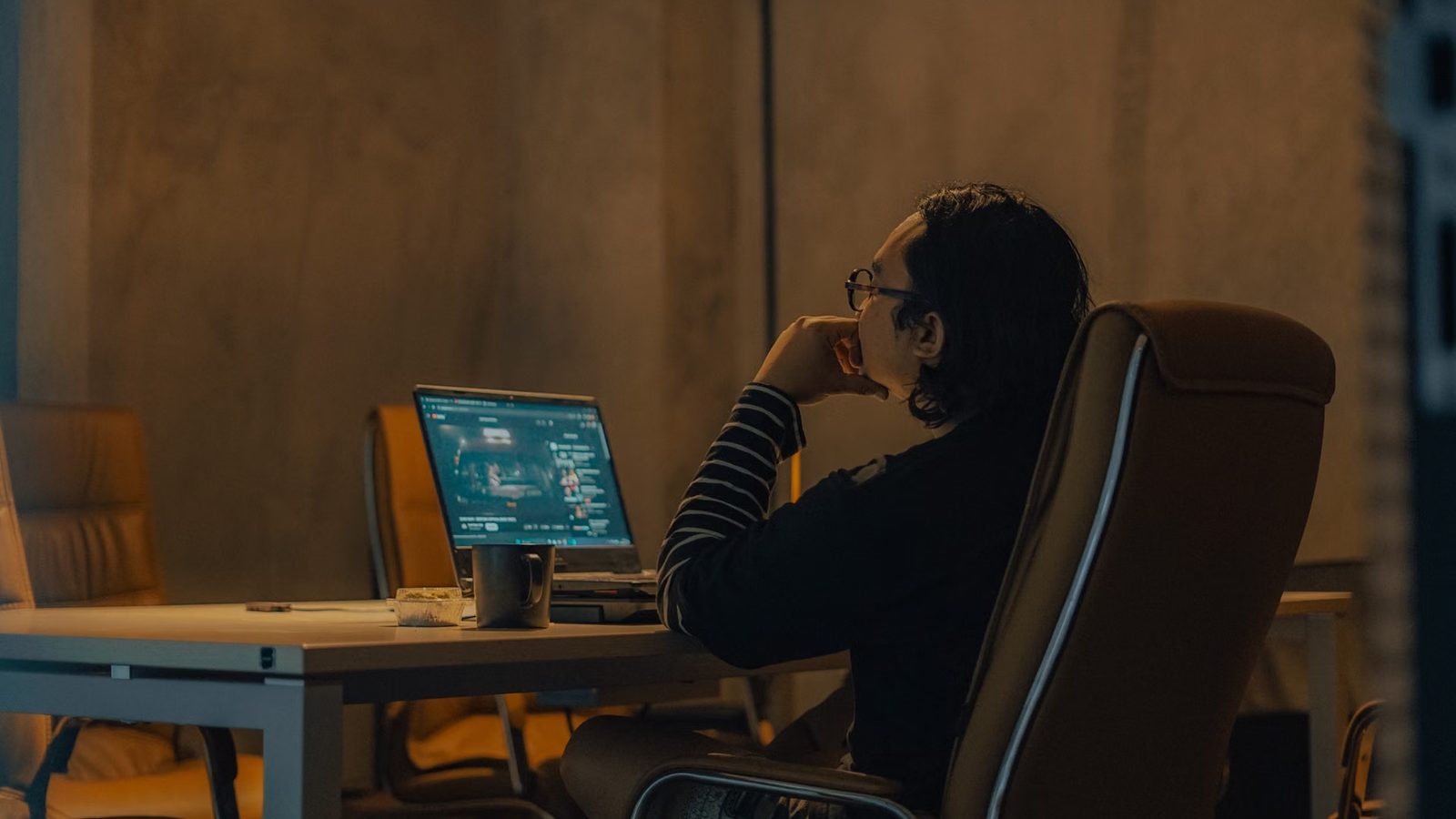 Mężczyzna siedzi wieczorem przy laptopie w biurze oświetlonym ciepłym światłem