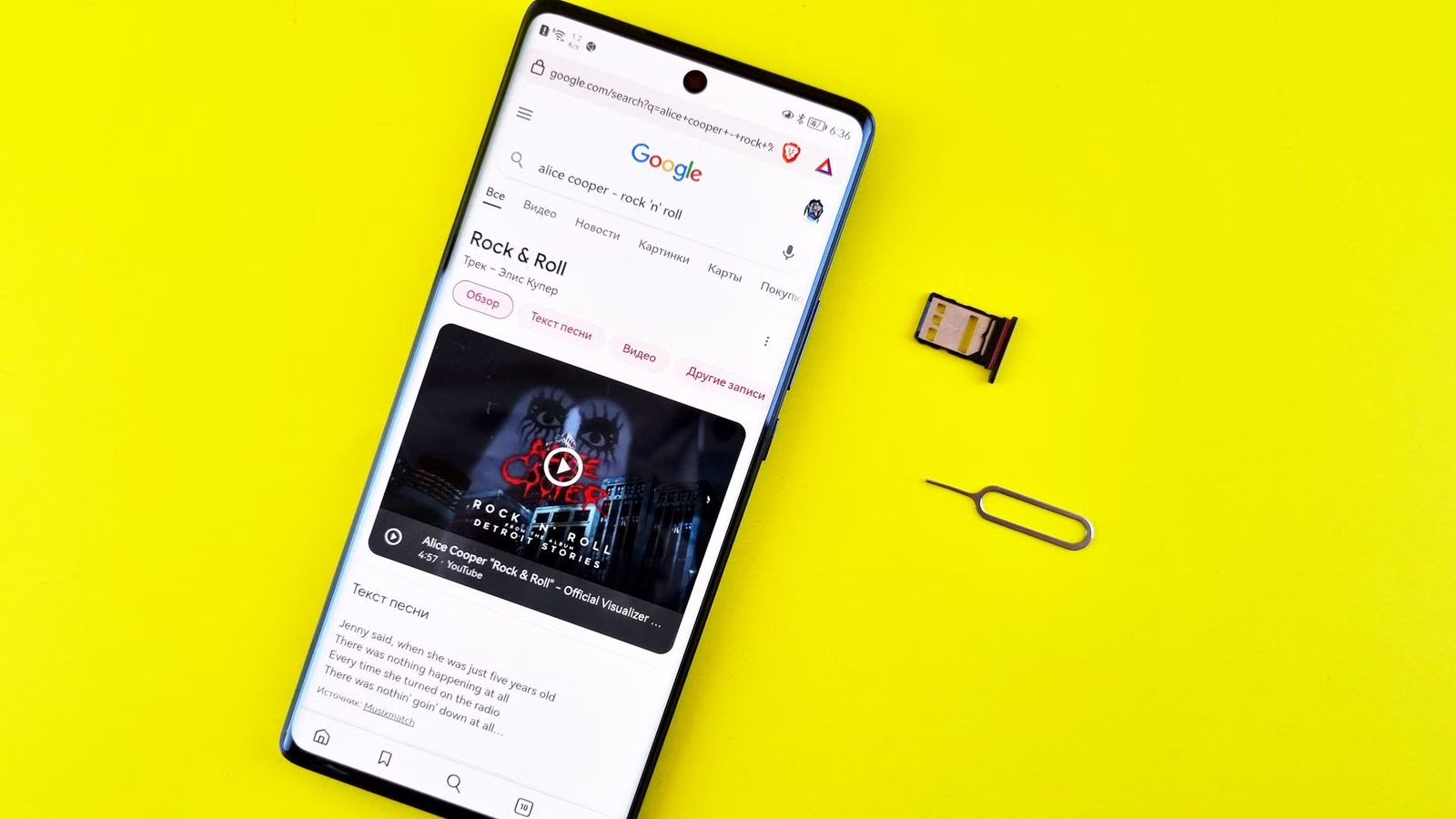 Smartfon leżący na żółtym tle z otwartą stroną wyników wyszukiwania Google, obok szuflada na kartę SIM