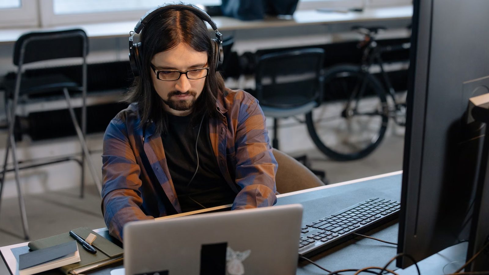 Mężczyzna w słuchawkach nausznych pracuje przy laptopie i monitorze w biurze