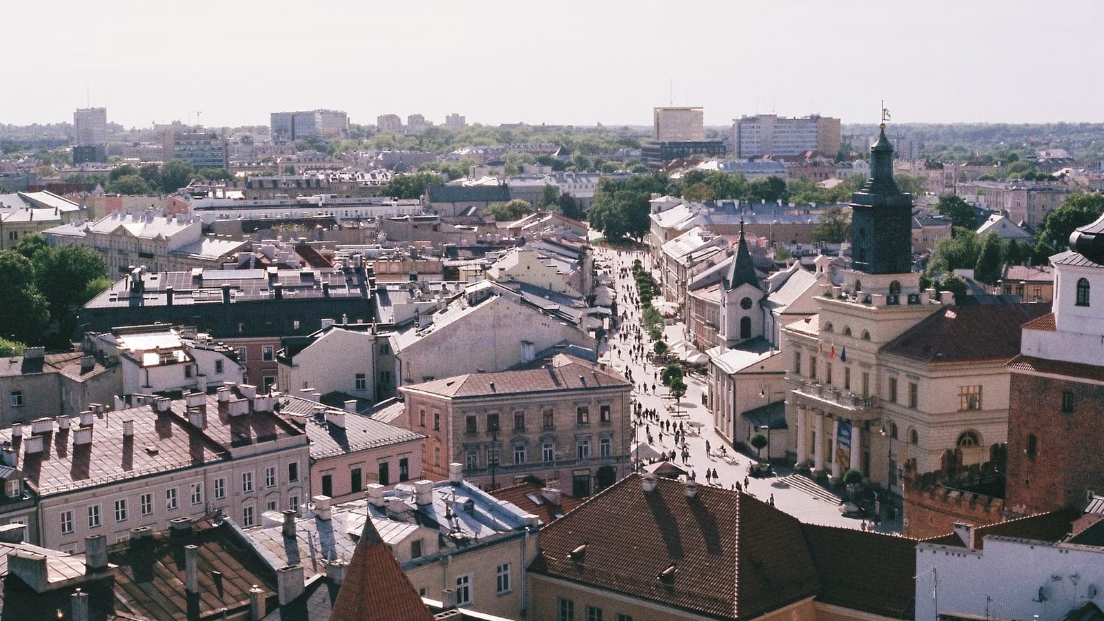 Widok z góry na kamienice starego miasta, wieżę ratusza i deptak z przechodniami