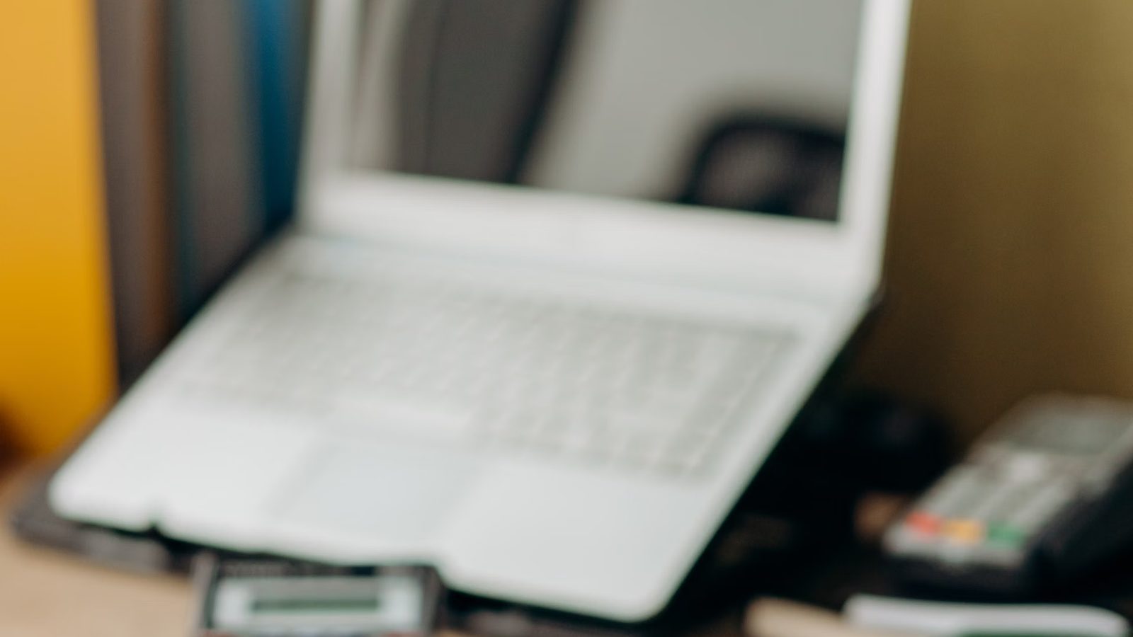 Nieostry kadr białego laptopa na biurku obok terminala płatniczego