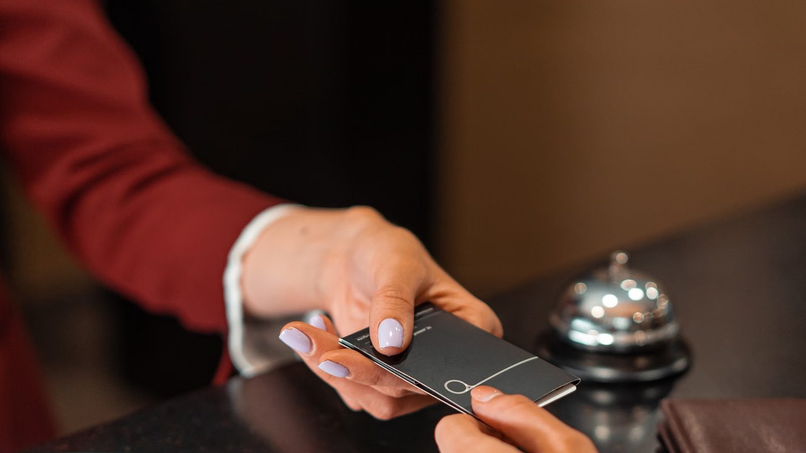 Recepcja hotelowa: dłoń podaje gościowi kartę do pokoju, obok dzwonek na blacie