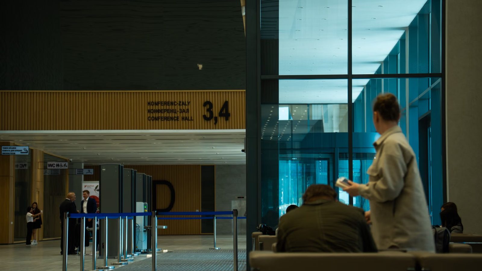 Osoby czekają na ławkach w holu centrum konferencyjnego