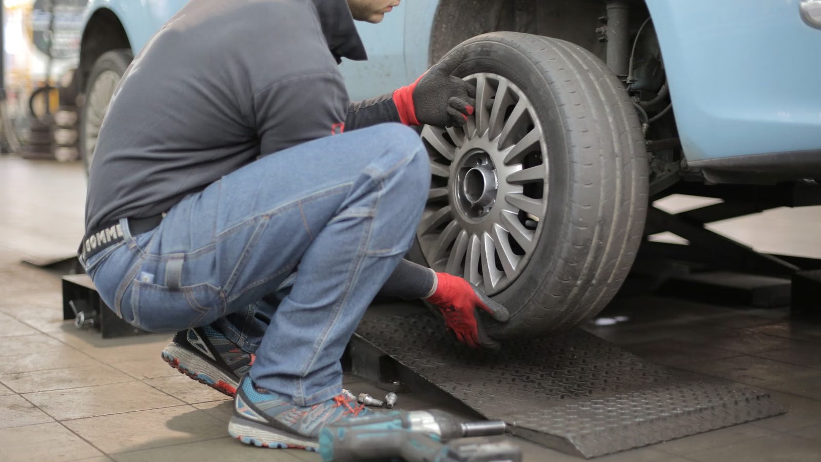 Mechanik w czerwonych rękawicach zdejmuje koło samochodu na podnośniku w warsztacie