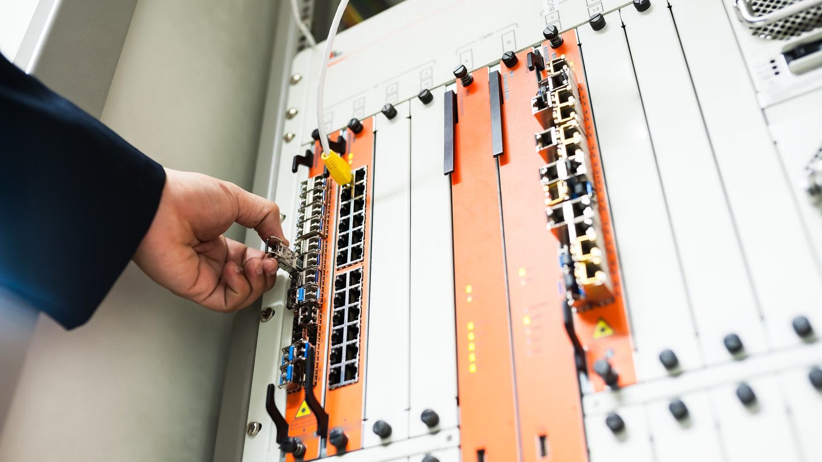 Dłoń przy module z portami sieciowymi w szafie telekomunikacyjnej