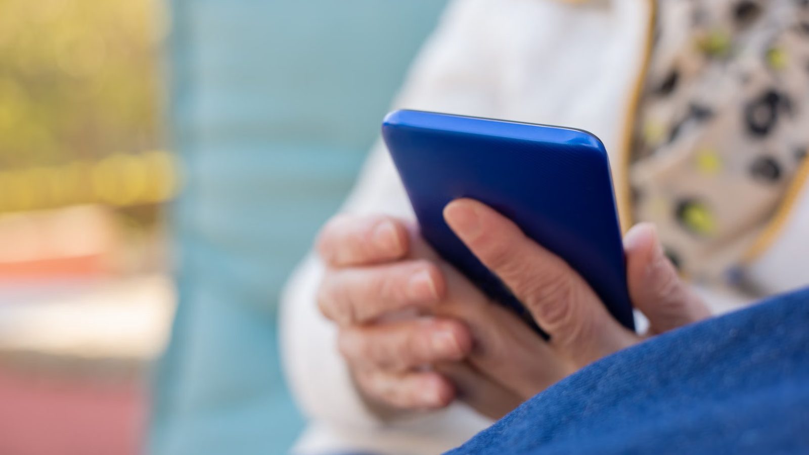 Dłonie starszej osoby trzymające niebieski smartfon