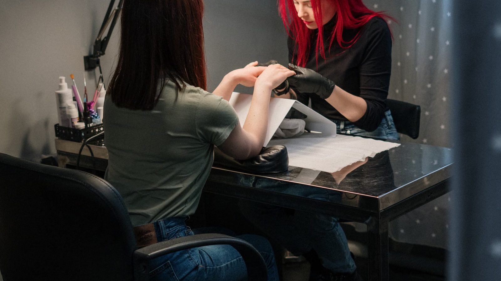 Stylistka w czarnych rękawiczkach wykonuje manicure klientce w salonie