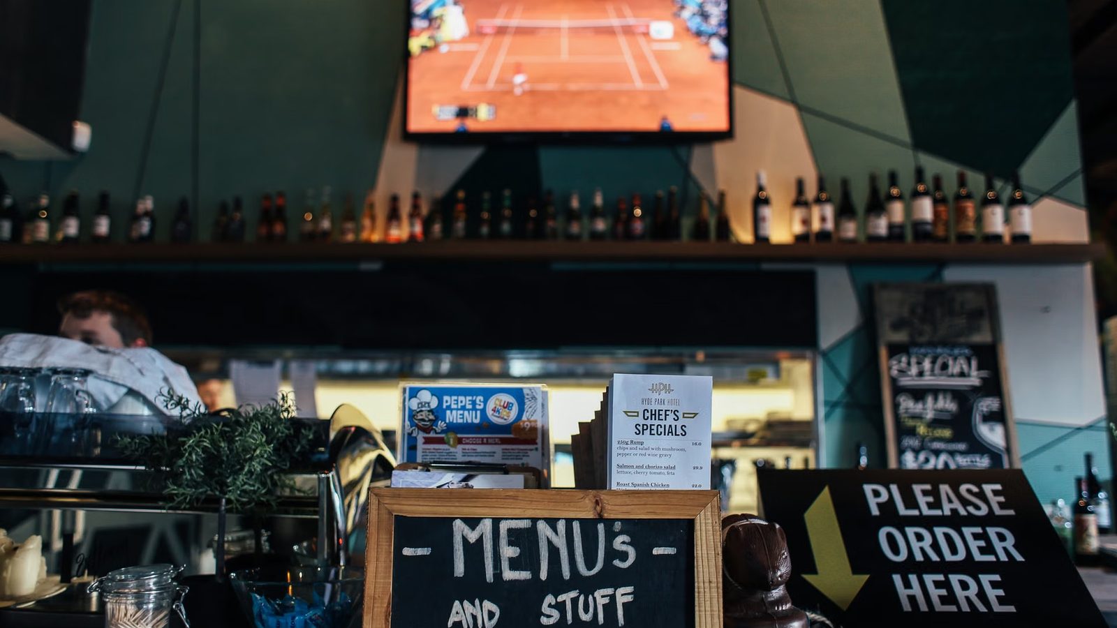 Karty menu i tablica kredowa na ladzie baru, w tle półka z butelkami