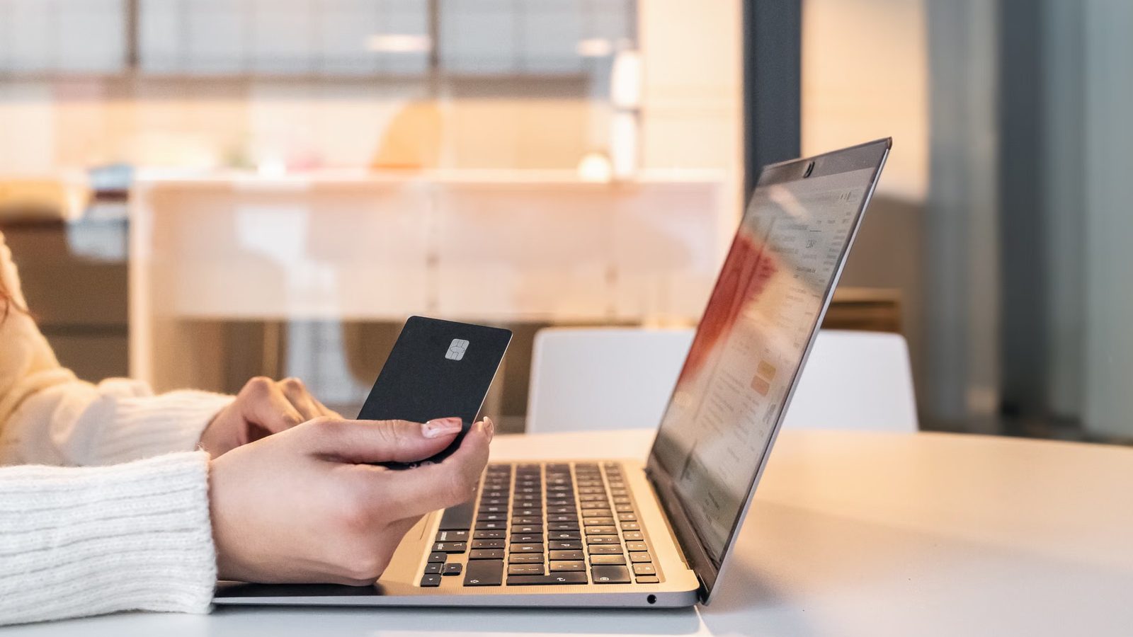 Dłoń z kartą płatniczą przy laptopie podczas zakupów online