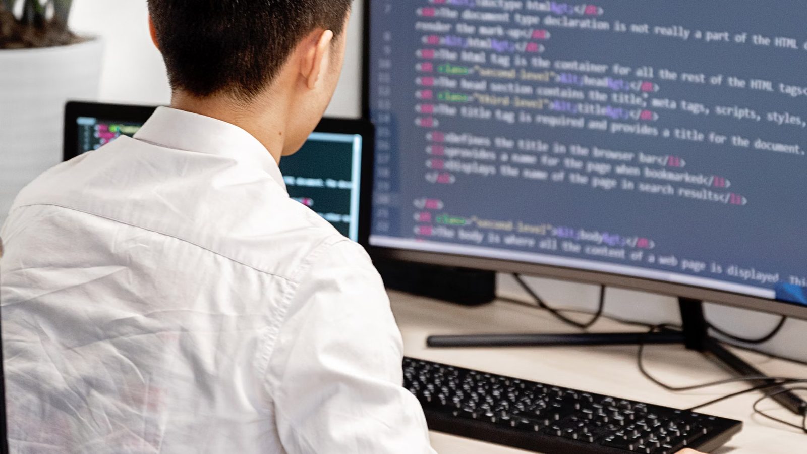 Programista w białej koszuli przy dużym monitorze z kodem HTML strony