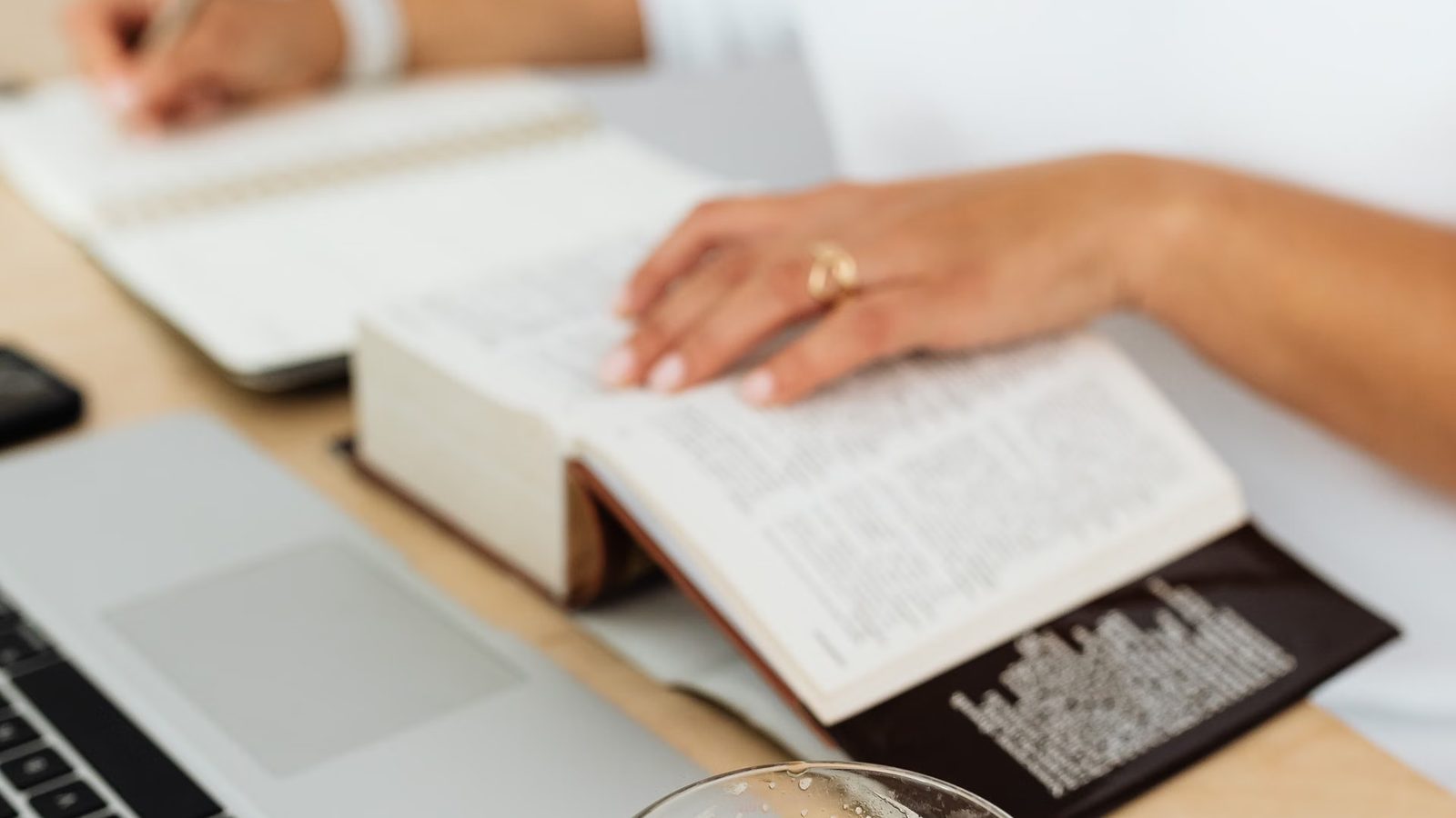 Osoba robi notatki przy otwartej książce i laptopie