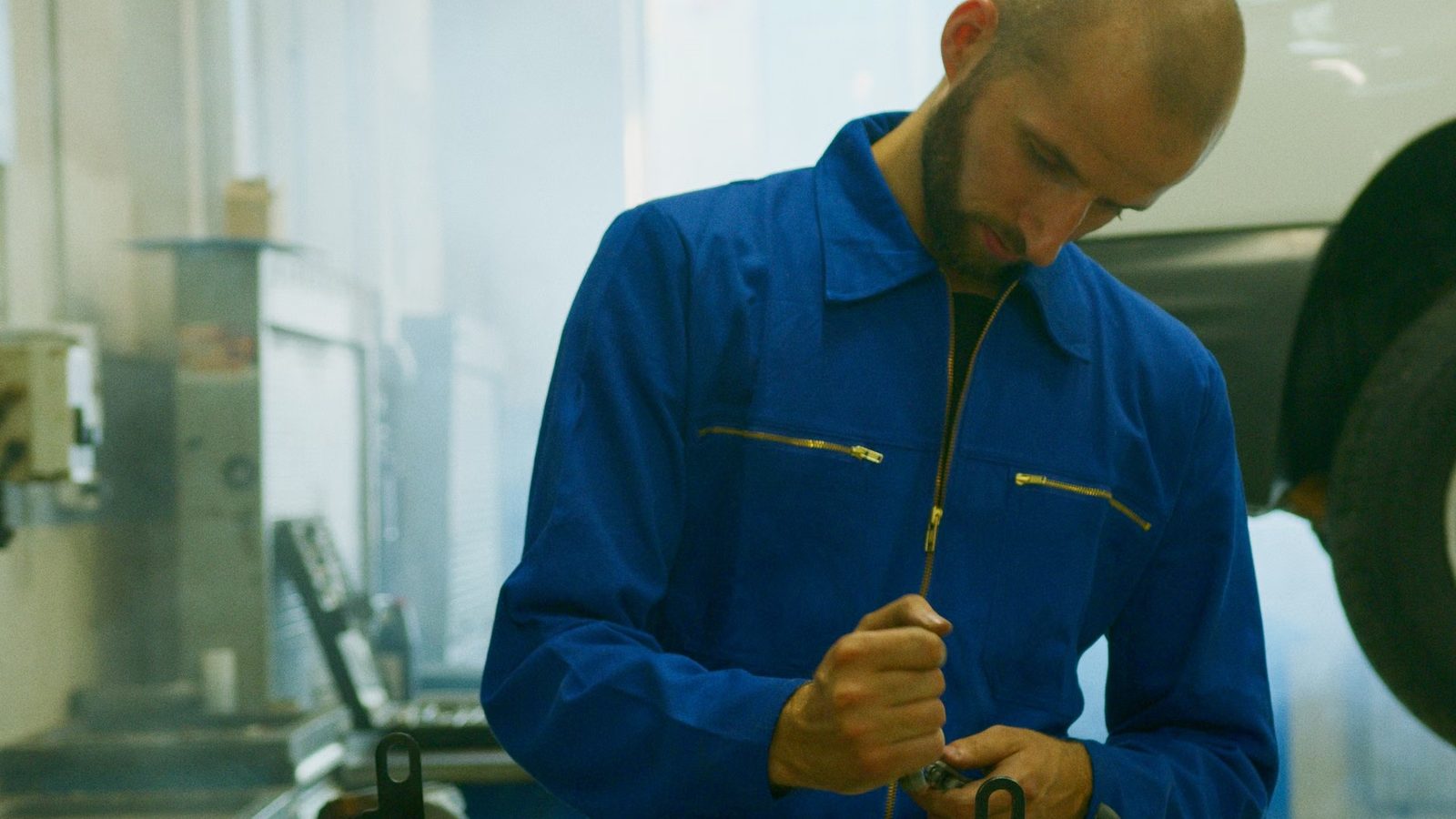 Mechanik w niebieskim kombinezonie ogląda małą metalową część w warsztacie samochodowym