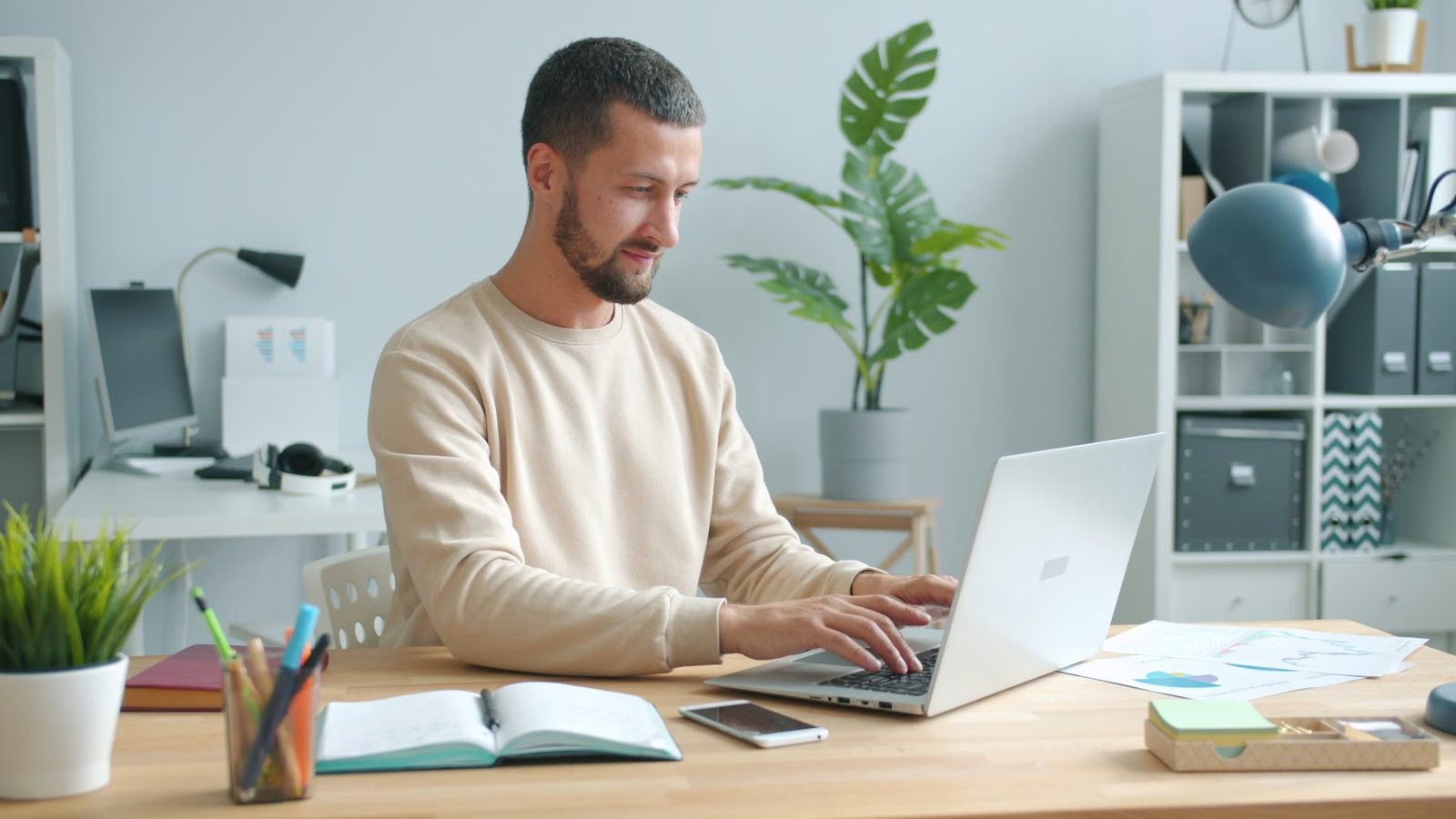 Mężczyzna pracuje przy laptopie w jasnym biurze z roślinami