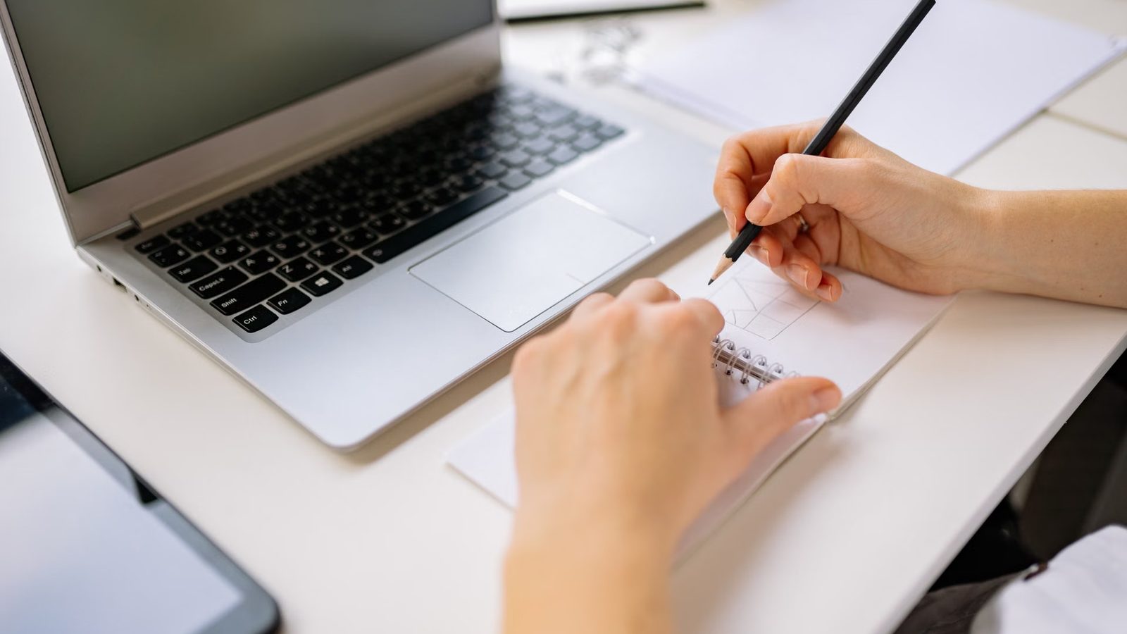Szkicowanie układu strony ołówkiem w notesie obok laptopa