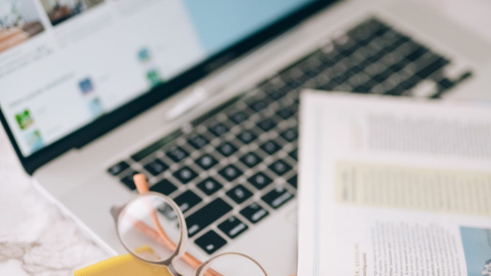 Okulary i wydrukowany artykuł leżą na klawiaturze otwartego laptopa